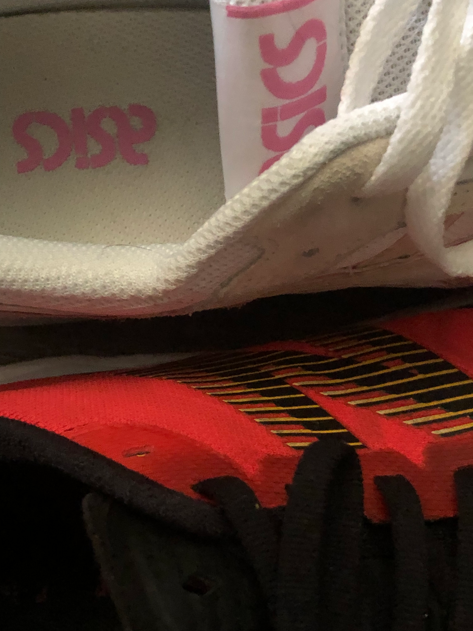 close-up photo of two shoes, one white with pink lettering, "asics", the other pink with the letter "N" in black and yellow. taken at the robledo art, strike! headquarters, february 2023.